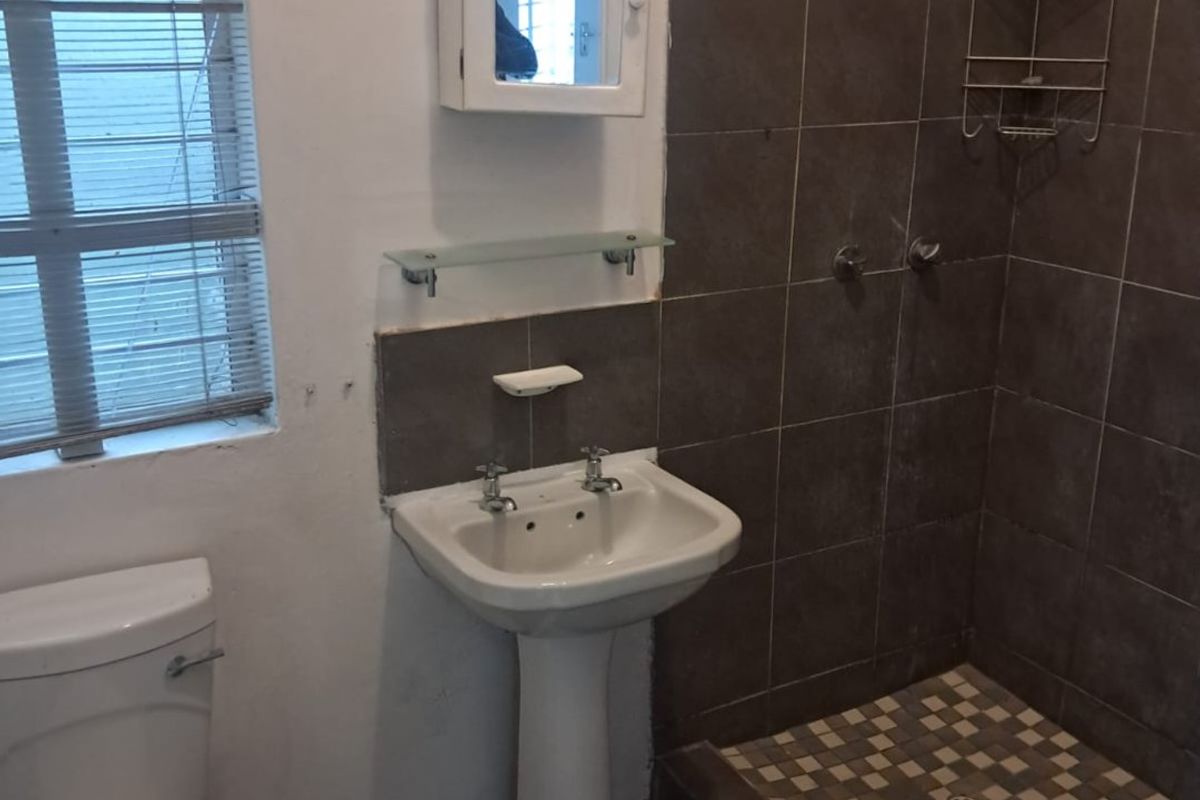 A functional bathroom featuring a pedestal basin, toilet, and a tiled shower enclosure with dark wall tiles and a mosaic floor.