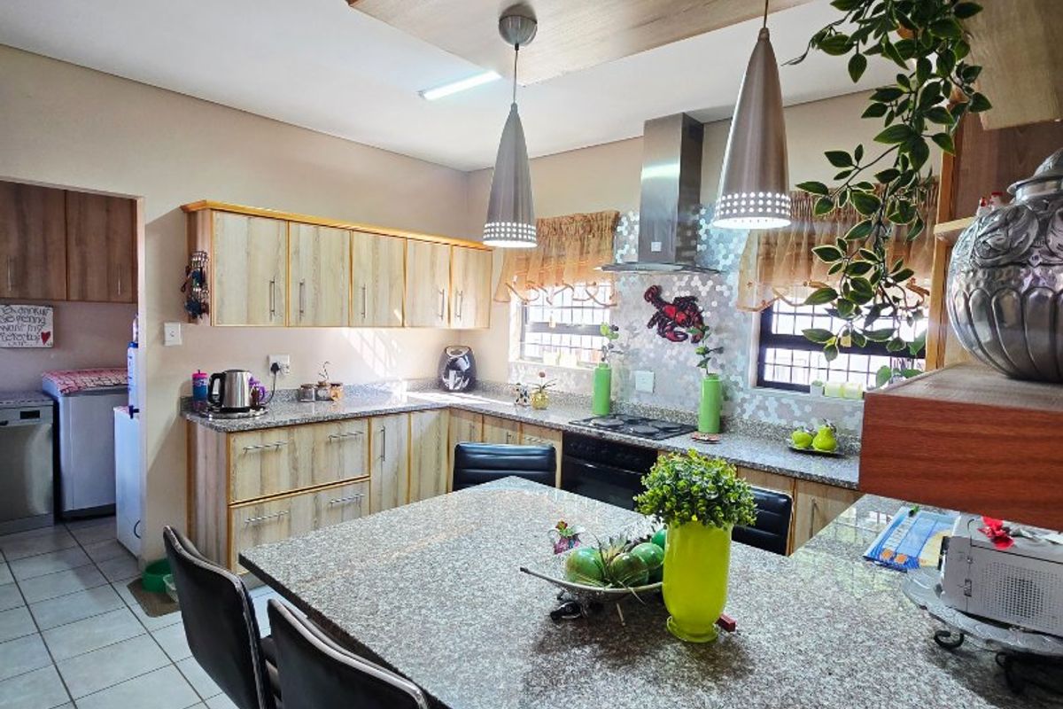 A well-maintained kitchen featuring granite countertops, built-in cabinetry, a breakfast bar, and modern pendant lighting, with an adjacent scullery area.