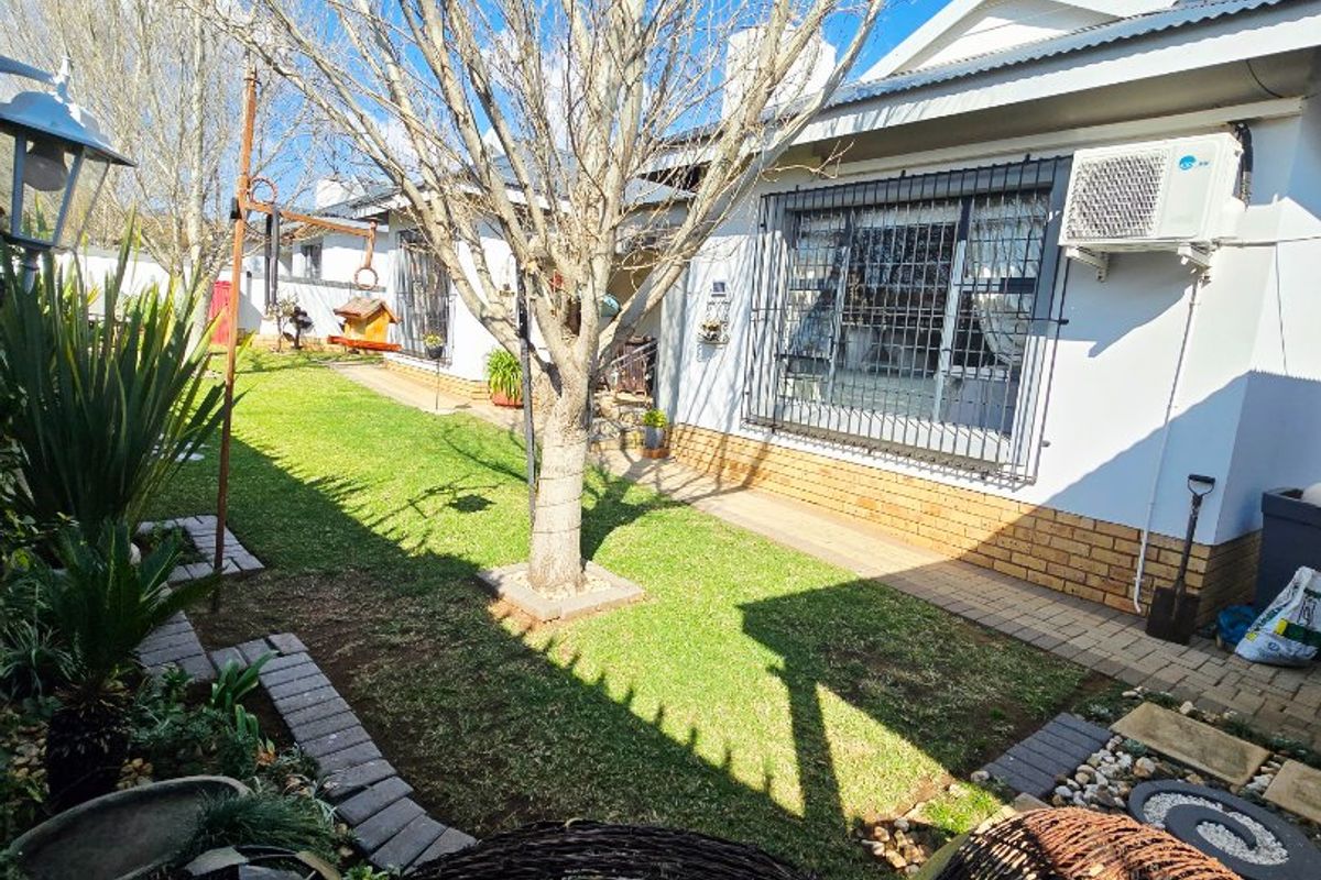 A well-maintained rear garden area featuring a lawn, paved pathways, and a building exterior equipped with security bars and an air conditioning unit.