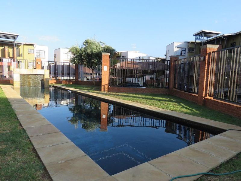 Communal swimming pool area featuring a water feature, paved surround, and secure brick and metal perimeter fencing within the apartment complex.