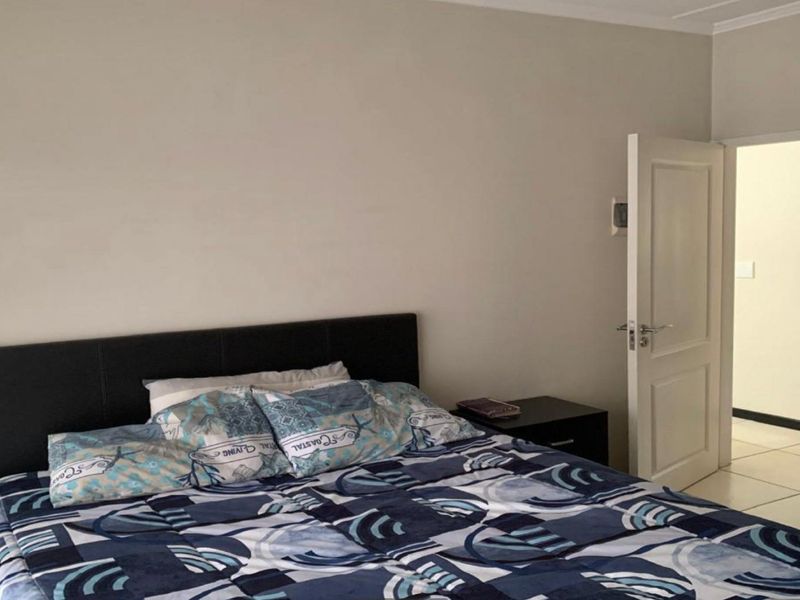 A functional bedroom featuring neutral wall finishes, tiled flooring, and a built-in wardrobe, offering a clean and simple living space.