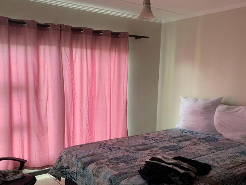 A functional bedroom featuring a window with curtain rod and ceiling lighting, providing a neutral space ready for personalization.
