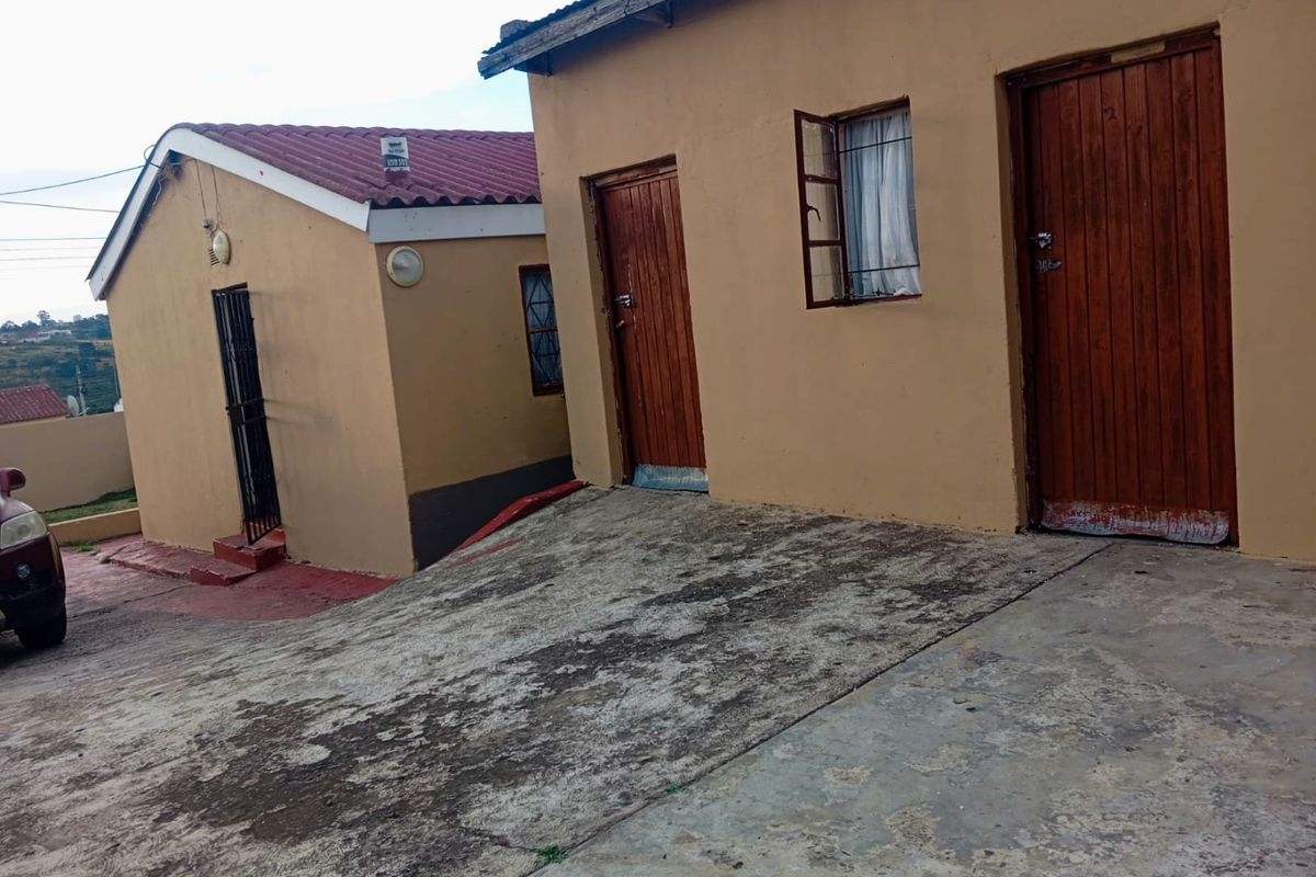 Exterior view of the property showing multiple entry points, concrete driveway, and basic building finishes.