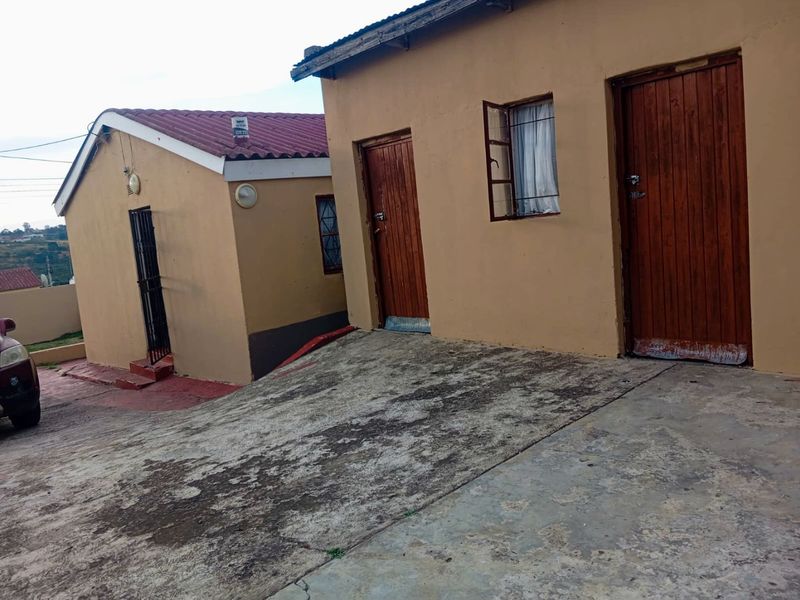 Exterior view of the property showing multiple entry points, concrete driveway, and basic building finishes.