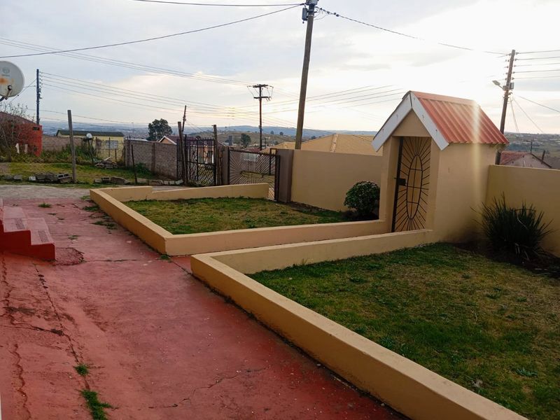 Rear yard area featuring raised garden beds, a small outbuilding, and concrete paving enclosed by a perimeter wall.