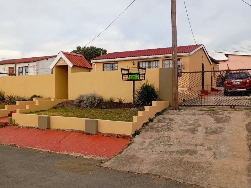 Front view of a single-story house featuring a perimeter wall, gated driveway, and tiled roof in a residential setting.