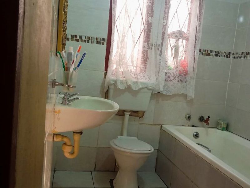 A dated bathroom featuring a wall-mounted basin, toilet, and bathtub with tiled finishes, requiring cosmetic updates and maintenance to improve its overall condition.