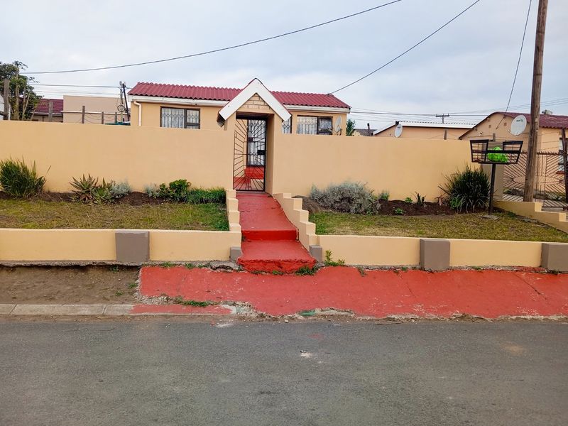 Front view of a residential property featuring a perimeter wall, security gate, and tiled roof, with a paved entrance path from the street.