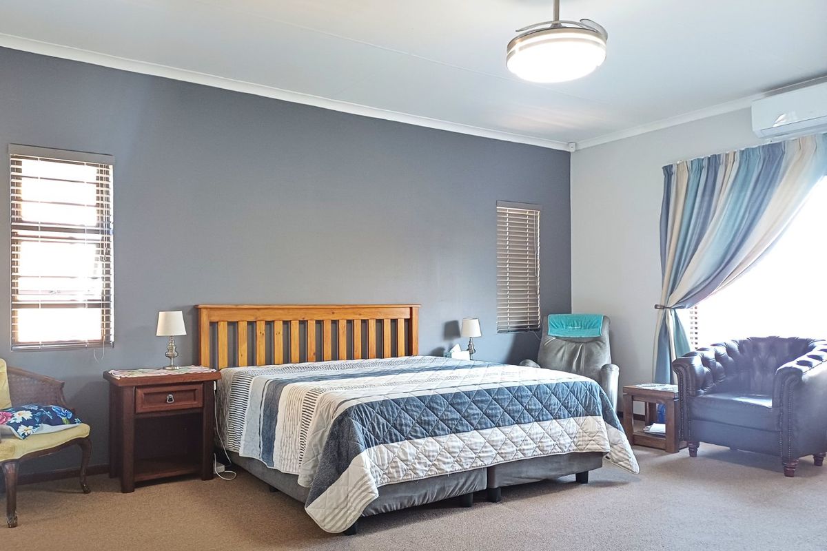 Spacious bedroom featuring neutral wall tones, carpeted flooring, a ceiling fan, and a wall-mounted air conditioning unit for climate control.