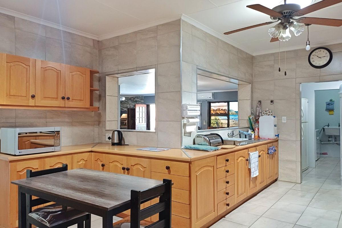 A functional kitchen featuring wooden cabinetry, tiled splashbacks, and a ceiling fan, with an open layout connecting to adjacent living spaces.