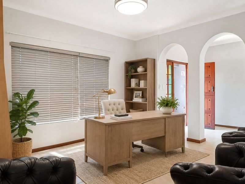 A bright and well-maintained home office featuring arched architectural details, tiled flooring, and large windows with venetian blinds.