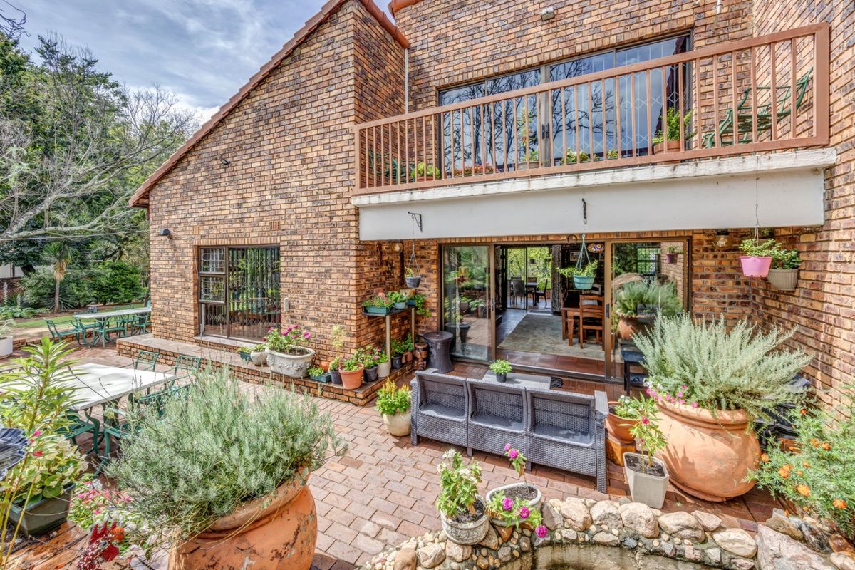 Rear view of a double-story brick house featuring a paved patio, a stone-edged water feature, and an upper-level balcony with sliding door access.