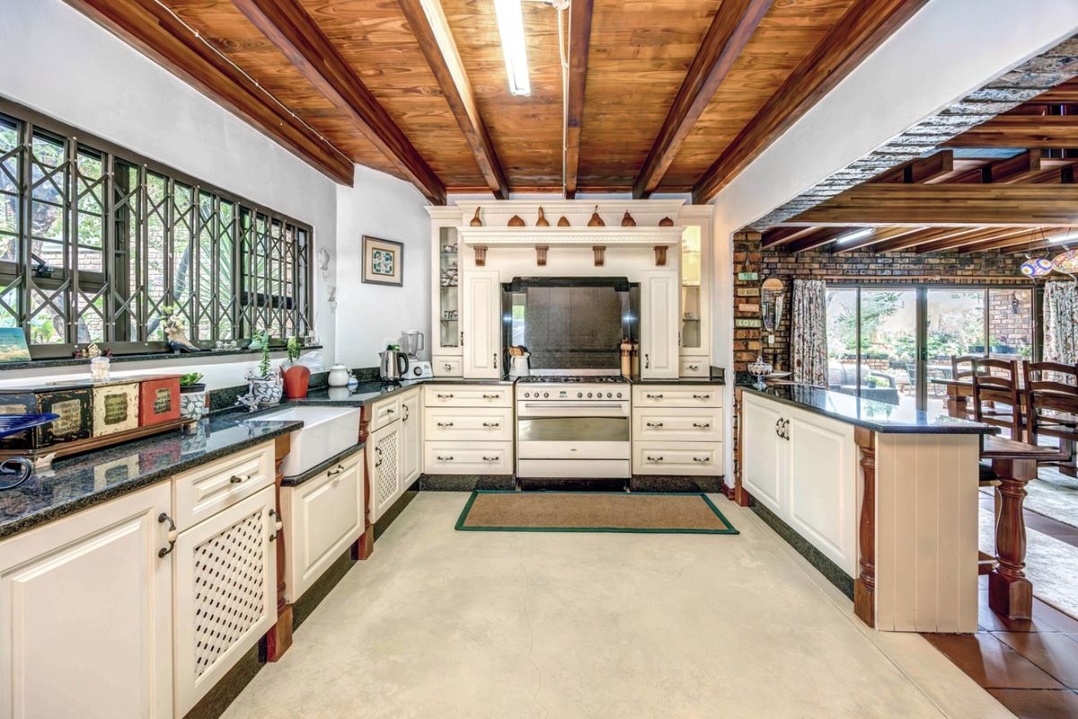 Spacious kitchen featuring farmhouse sink, granite countertops, freestanding gas range, and distinctive exposed timber ceiling beams with an open-plan layout.