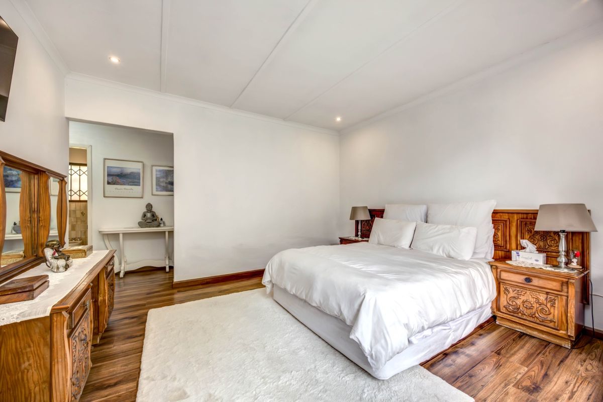 A well-maintained bedroom featuring laminate wood flooring, recessed ceiling lighting, and a neutral color palette, with an adjoining dressing or vanity area.