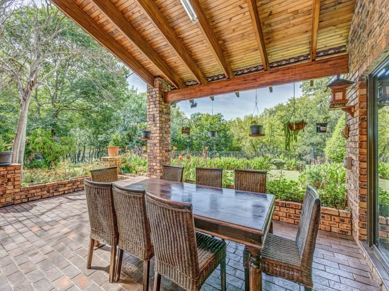 A covered outdoor patio featuring exposed timber beam ceilings, brick pillars, and built-in brick planter boxes overlooking a lush garden.