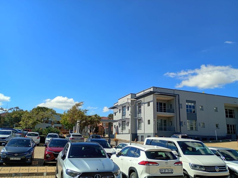 Exterior view of a modern multi-story commercial office building with an adjacent paved parking area.