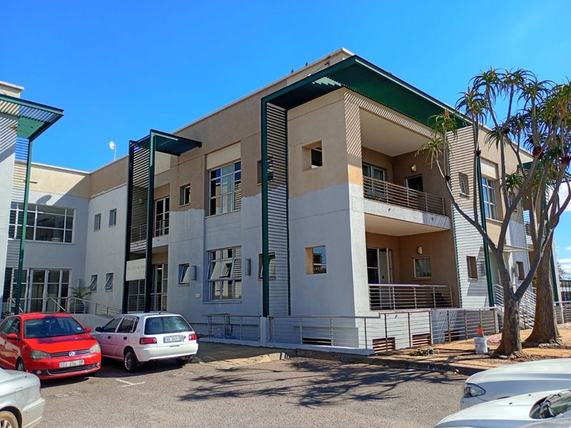 Exterior view of a commercial building featuring multi-level balconies, metal sunshades, and an adjacent paved parking area.