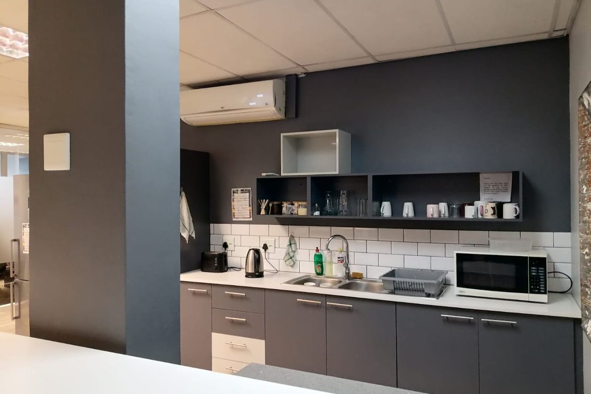 A functional office kitchenette featuring modern grey cabinetry, subway tile backsplash, stainless steel sink, and a wall-mounted air conditioning unit.