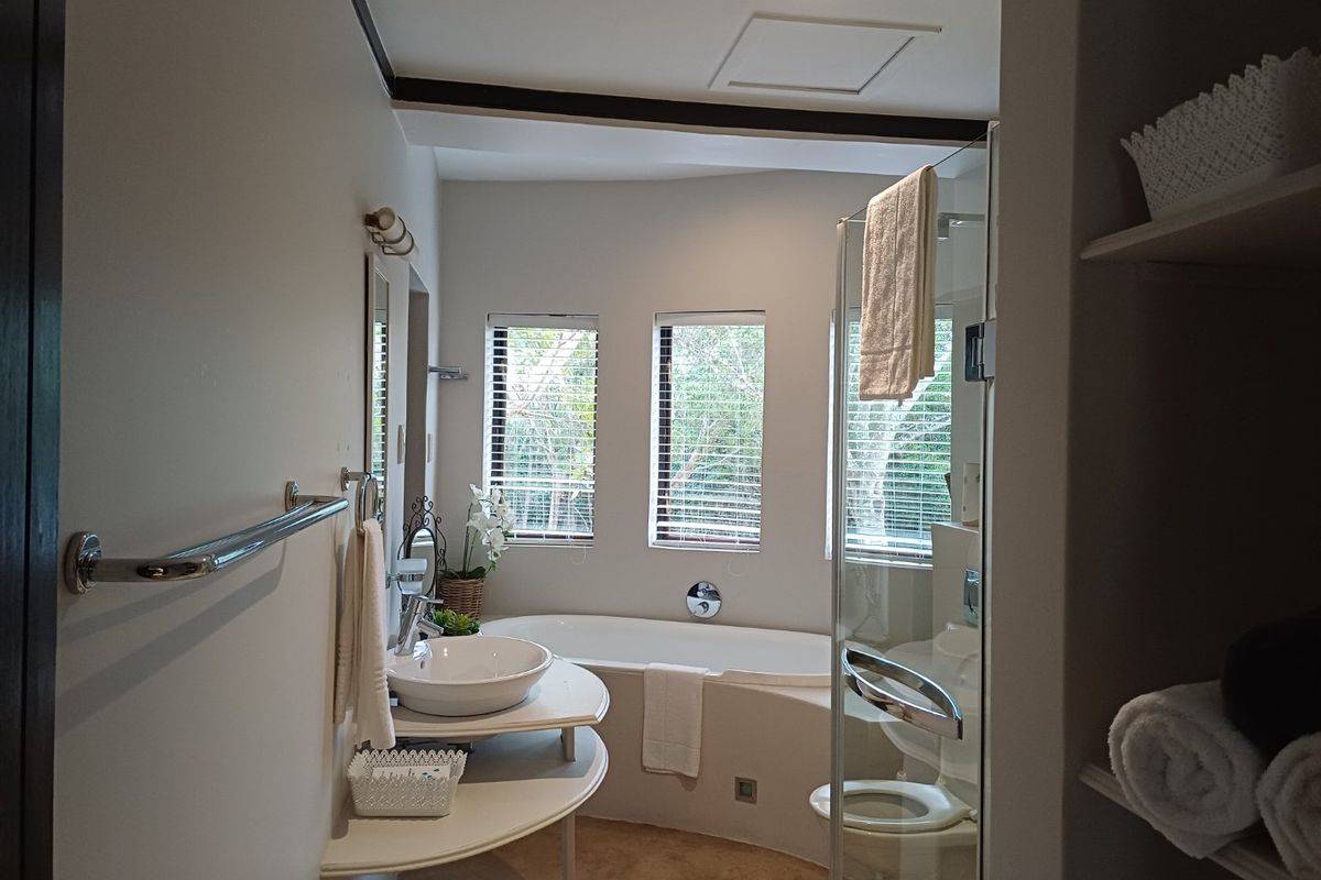 A well-lit bathroom featuring a vessel sink, a built-in bathtub, a glass-enclosed shower, and a toilet, with natural light provided by dual windows.