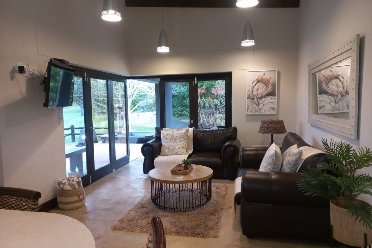 A bright living room featuring polished concrete floors, exposed ceiling beams, and large bi-fold glass doors providing seamless access to the outdoor patio area.