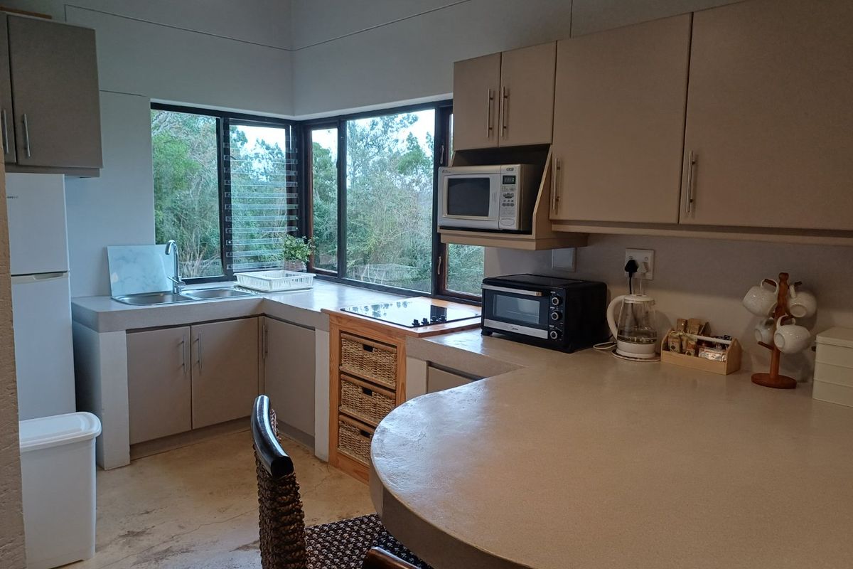 Functional kitchen featuring concrete countertops, built-in cabinetry, and a breakfast bar, with large windows providing natural light and garden views.