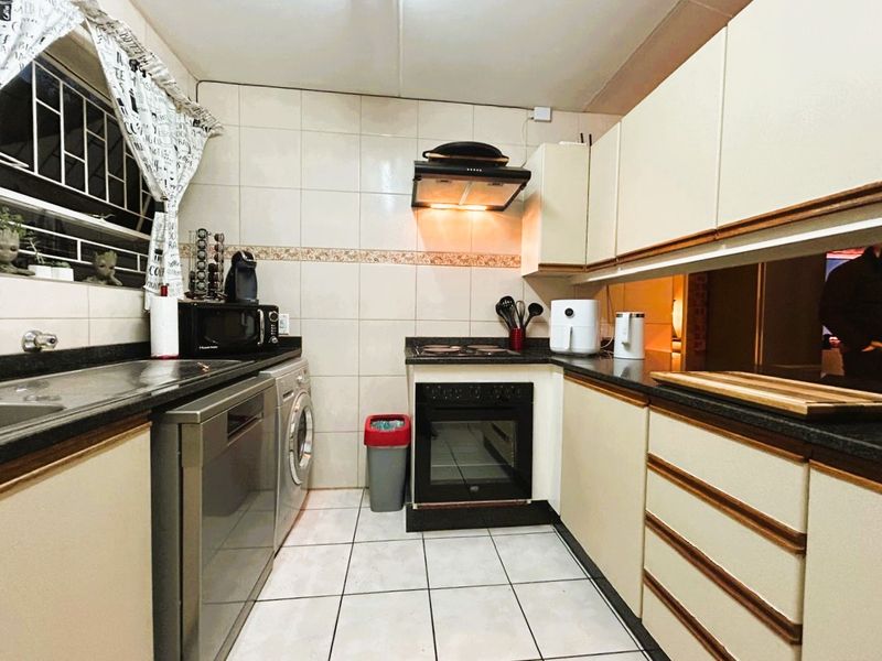 A functional kitchen featuring built-in cabinetry, granite countertops, an integrated oven with hob, extractor fan, and tiled finishes throughout.