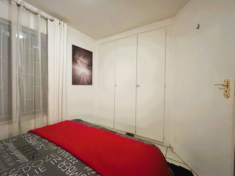 A bedroom featuring built-in cupboards, tiled flooring, and security bars on the window, providing a functional and secure living space.
