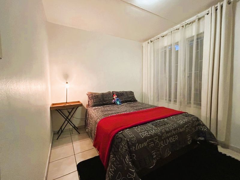 A functional bedroom featuring tiled flooring and a window fitted with security bars and curtains.