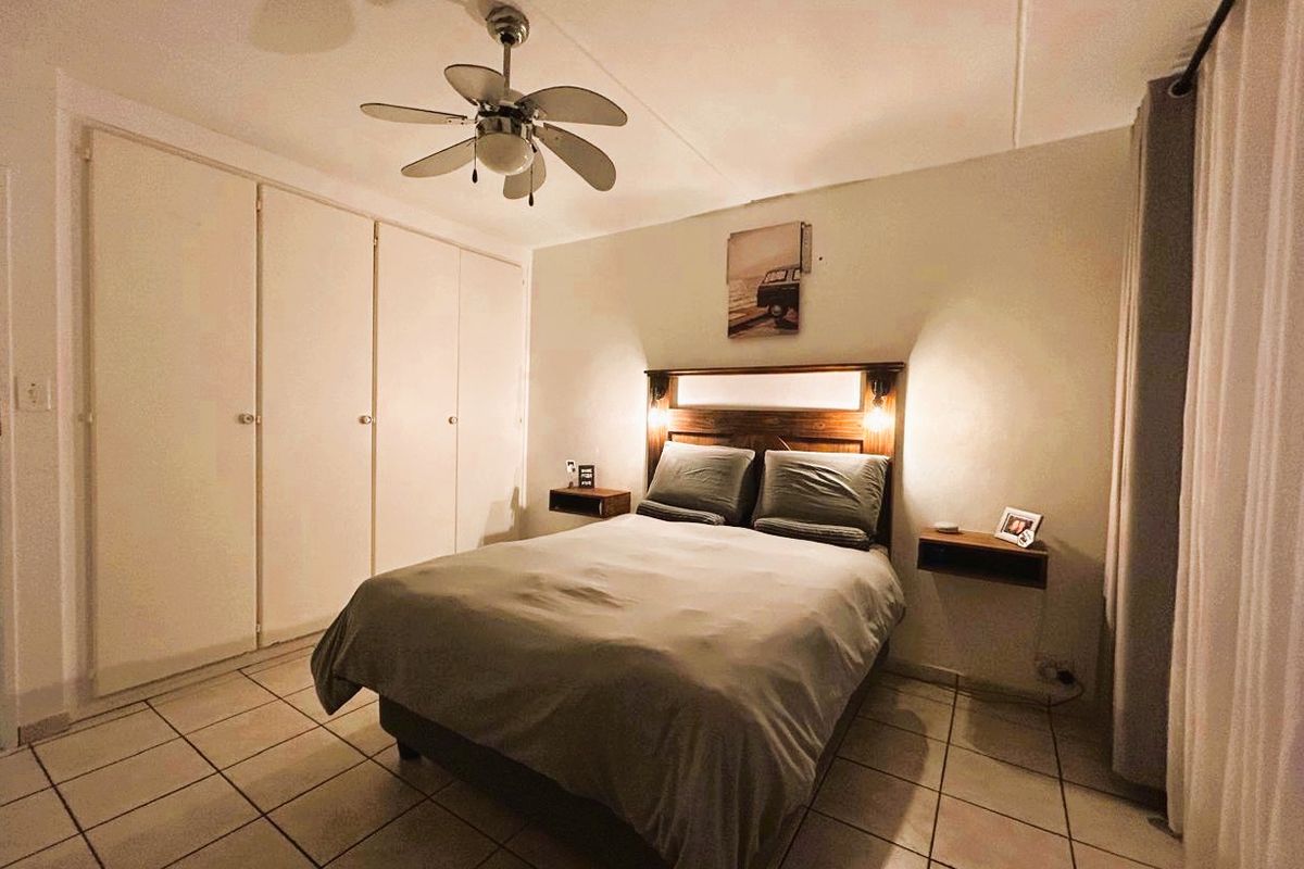 A bedroom featuring tiled flooring, built-in cupboards, and a ceiling fan, providing a functional and comfortable sleeping space.