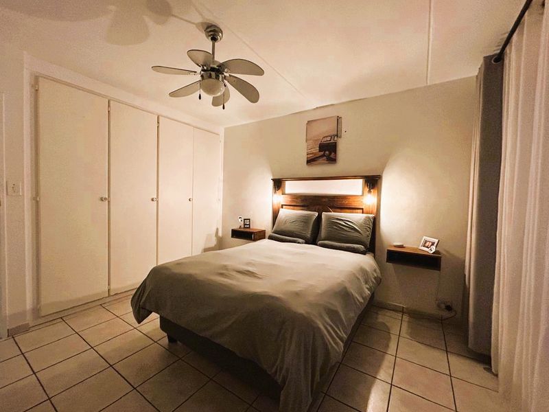 A bedroom featuring tiled flooring, built-in cupboards, and a ceiling fan, providing a functional and comfortable sleeping space.