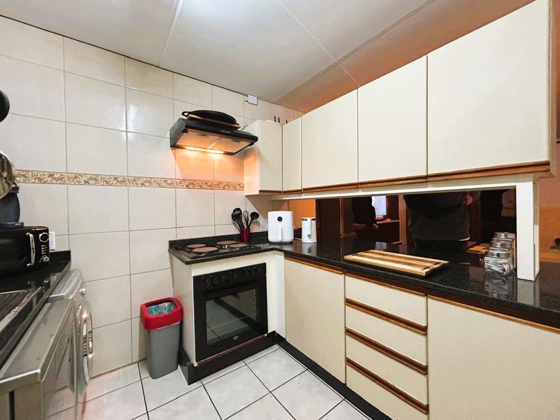 Compact kitchen featuring built-in cabinetry, granite countertops, an electric hob, oven, extractor fan, and tiled finishes throughout.