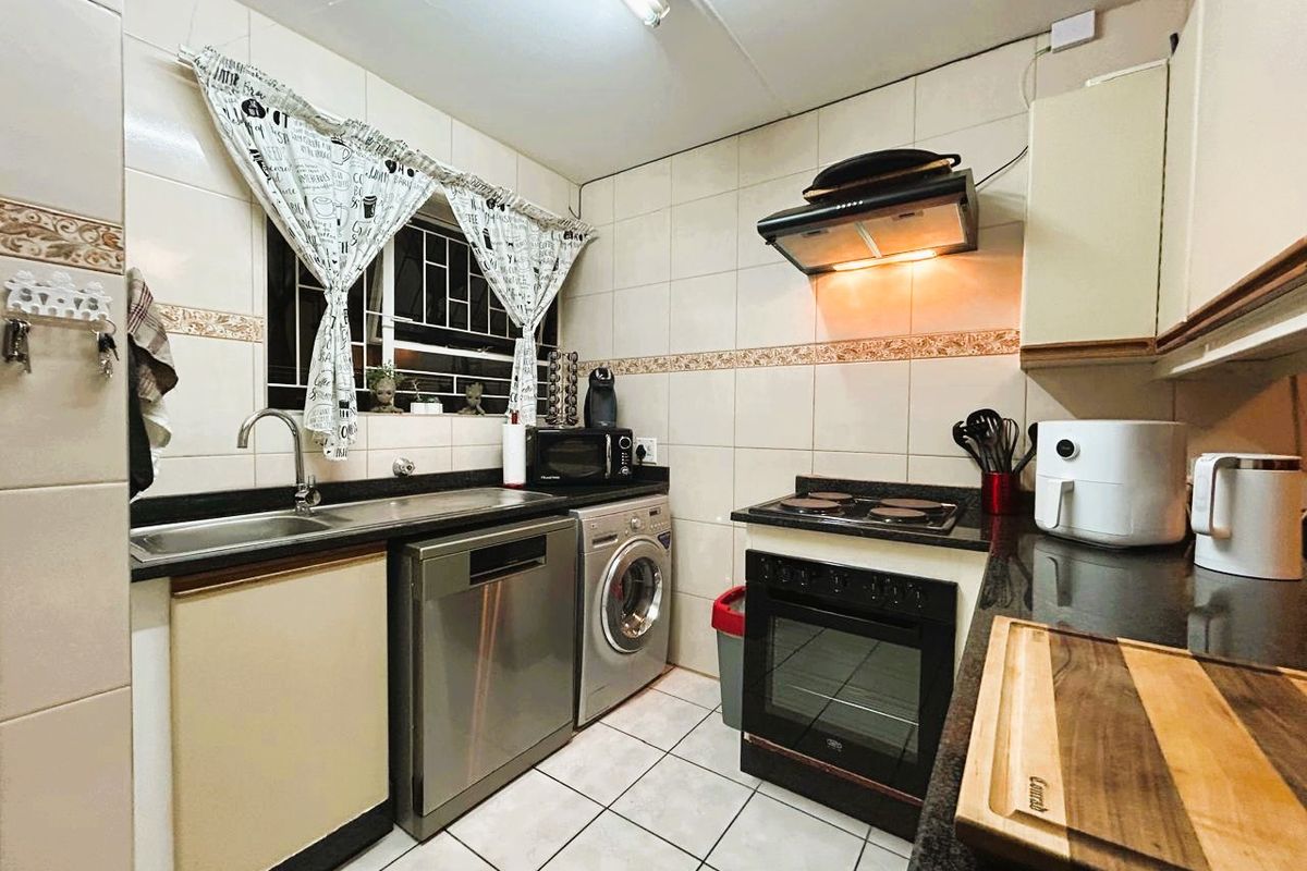 A functional kitchen featuring granite countertops, tiled splashbacks, built-in cabinetry, and integrated appliances including an oven, hob, and extractor fan.