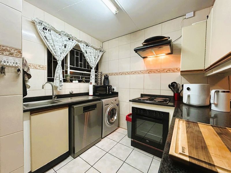 A functional kitchen featuring granite countertops, tiled splashbacks, built-in cabinetry, and integrated appliances including an oven, hob, and extractor fan.