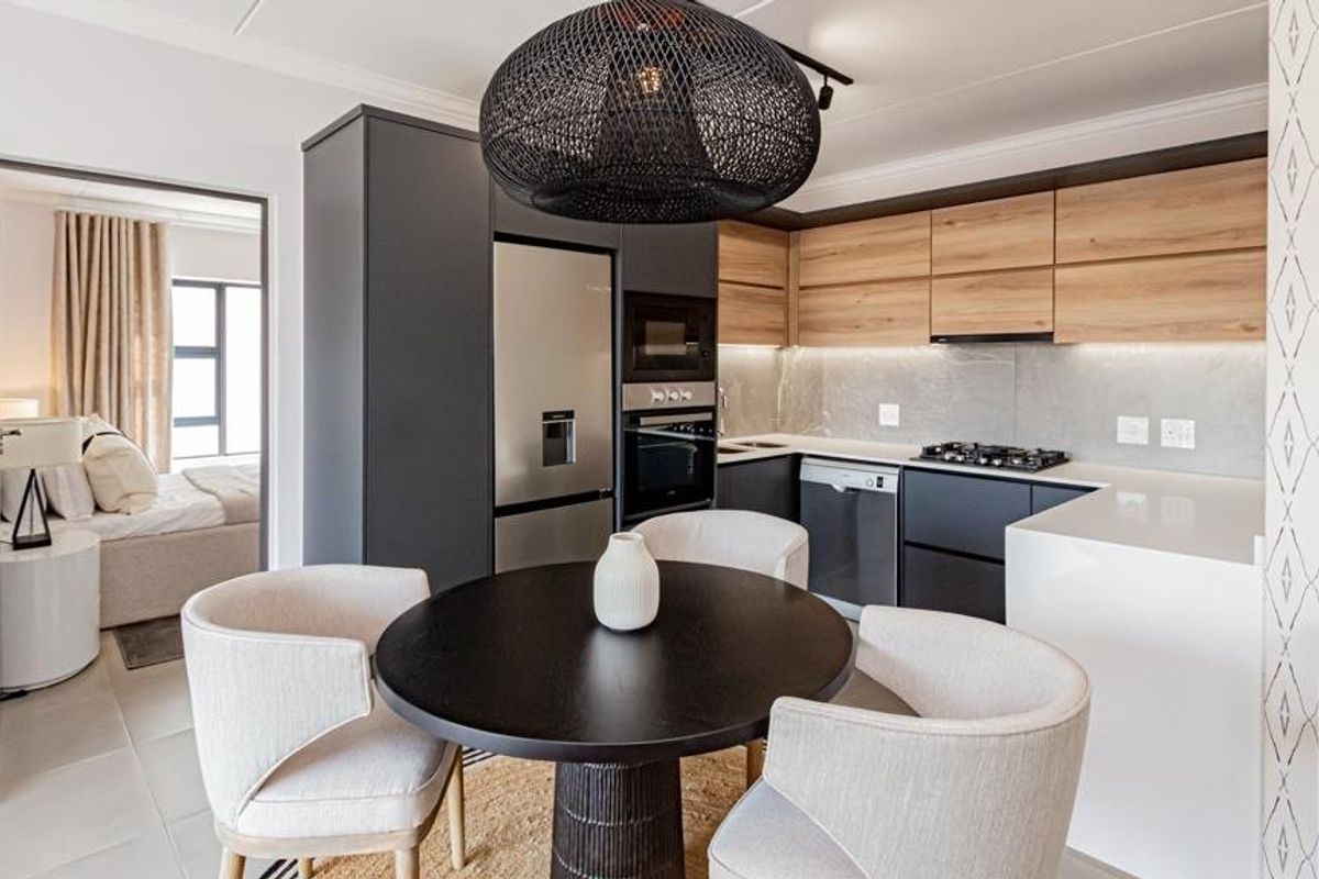 Modern open-plan kitchen featuring sleek dark cabinetry, wood-tone upper cabinets, stone countertops, and integrated appliances, seamlessly flowing into the adjacent living and bedroom areas.
