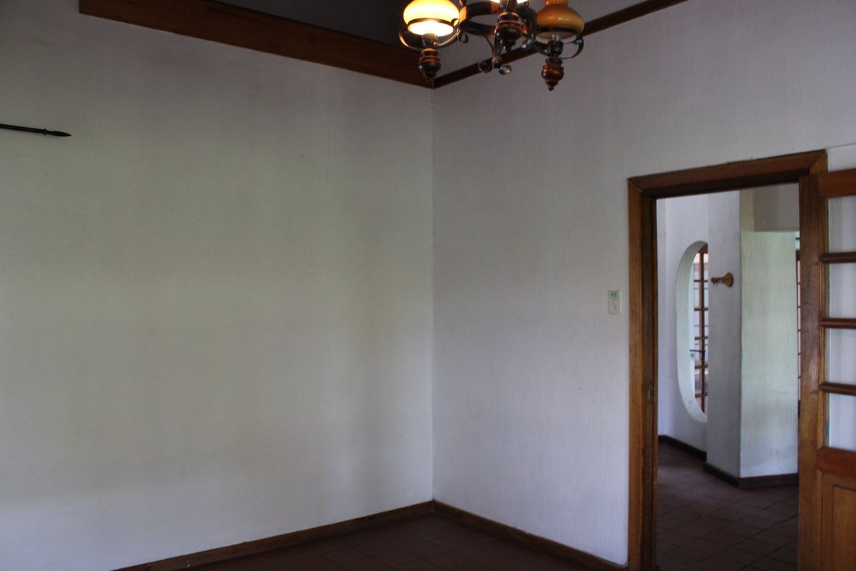 An empty living room featuring tiled flooring, timber ceiling trim, and a wooden door frame leading to an adjacent space with an archway.