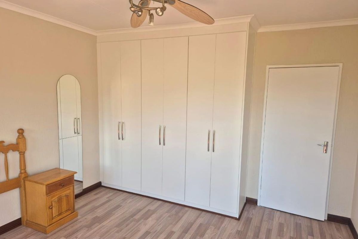 A well-maintained bedroom featuring modern white built-in cupboards, a ceiling fan, and durable laminate flooring.