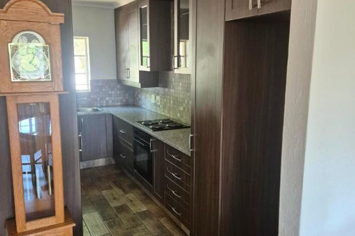 A functional kitchen featuring dark wood-finish cabinetry, granite countertops, a mosaic tile backsplash, and durable wood-look tile flooring.