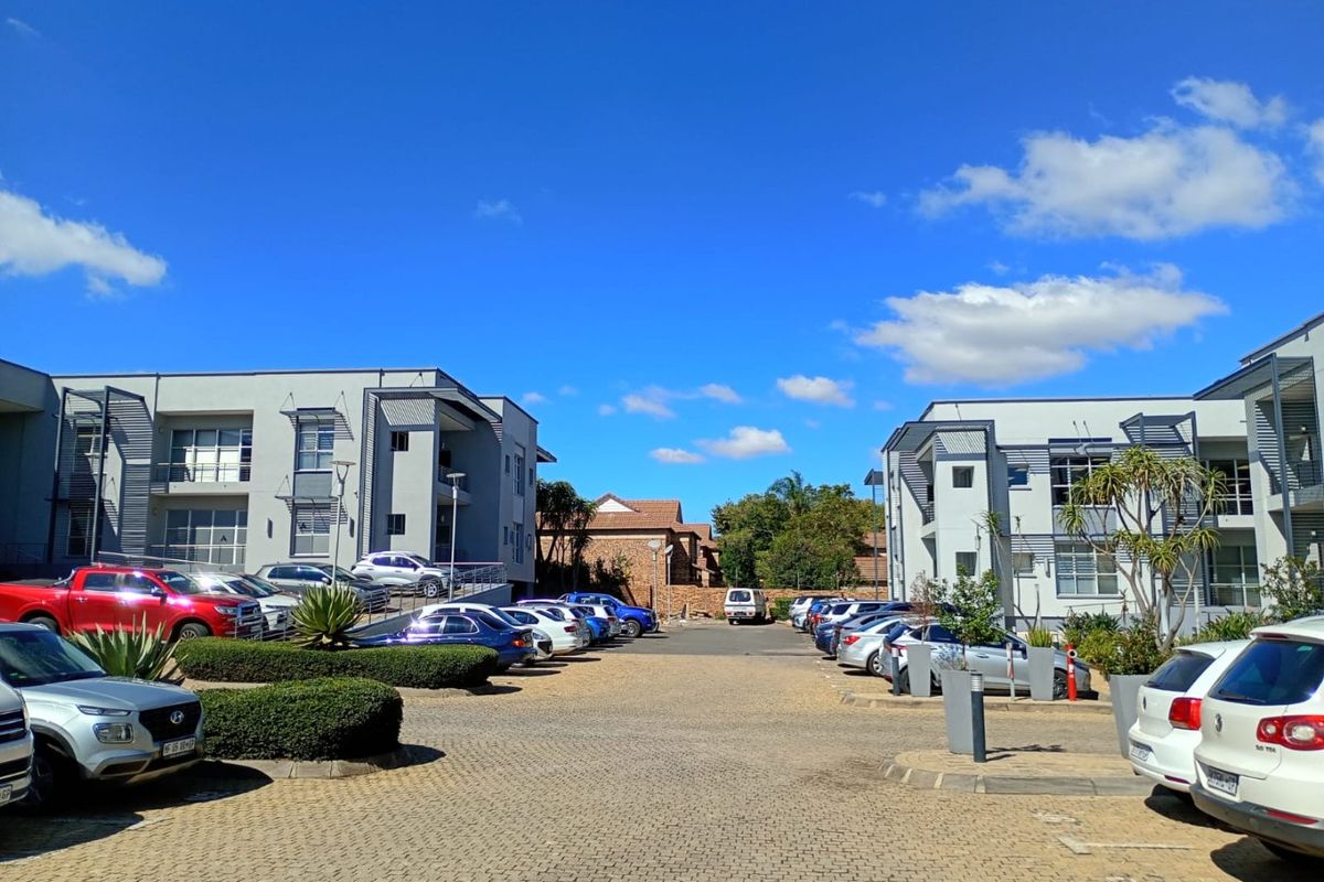 A view of the paved parking area and front facades of modern multi-story residential apartment buildings under a clear blue sky.