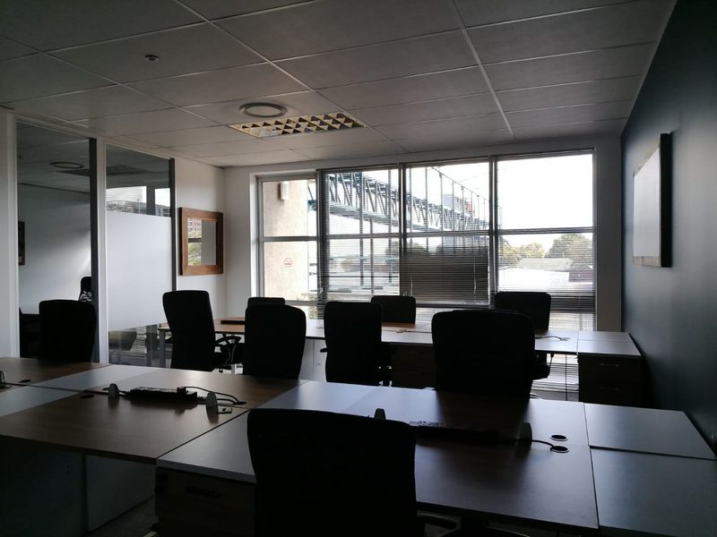 A functional office space featuring built-in desk workstations, a suspended ceiling with recessed lighting, and large windows providing natural light.