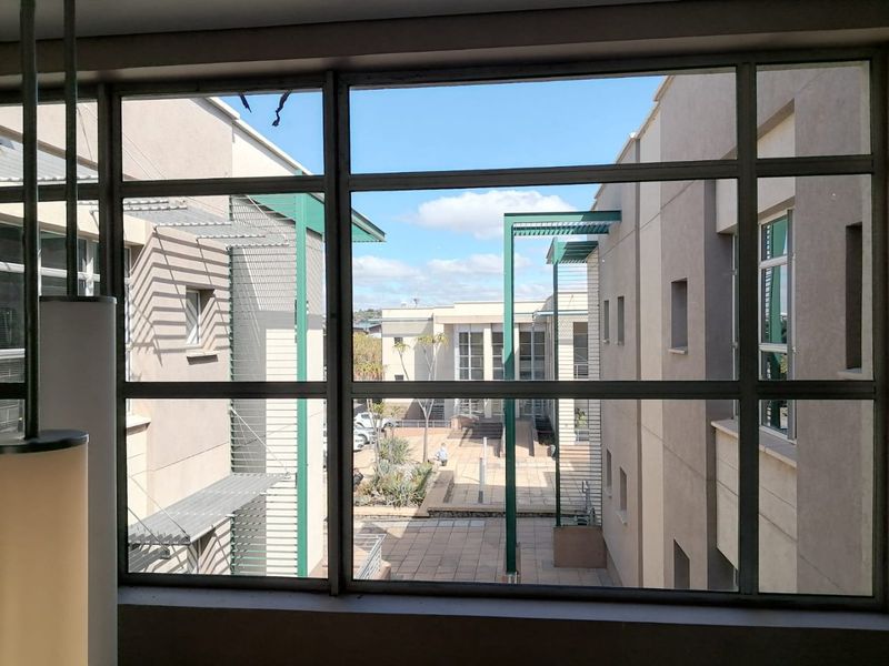 A view through a large metal-framed window looking out over a paved courtyard between modern residential building blocks.
