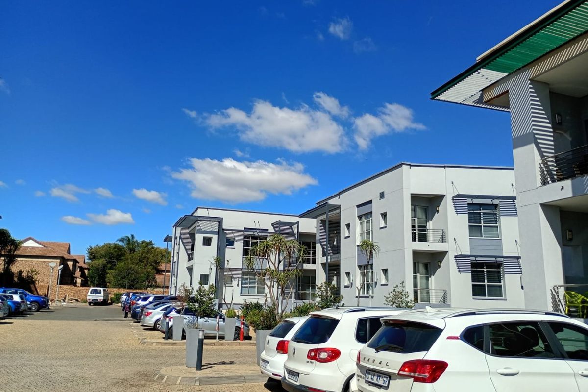 Exterior view of a modern multi-story residential complex with paved parking area and clear blue sky.
