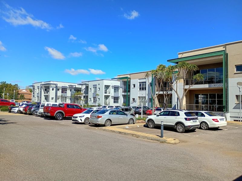 Exterior view of a modern multi-story commercial office complex featuring a paved parking area and contemporary building facade with balconies.