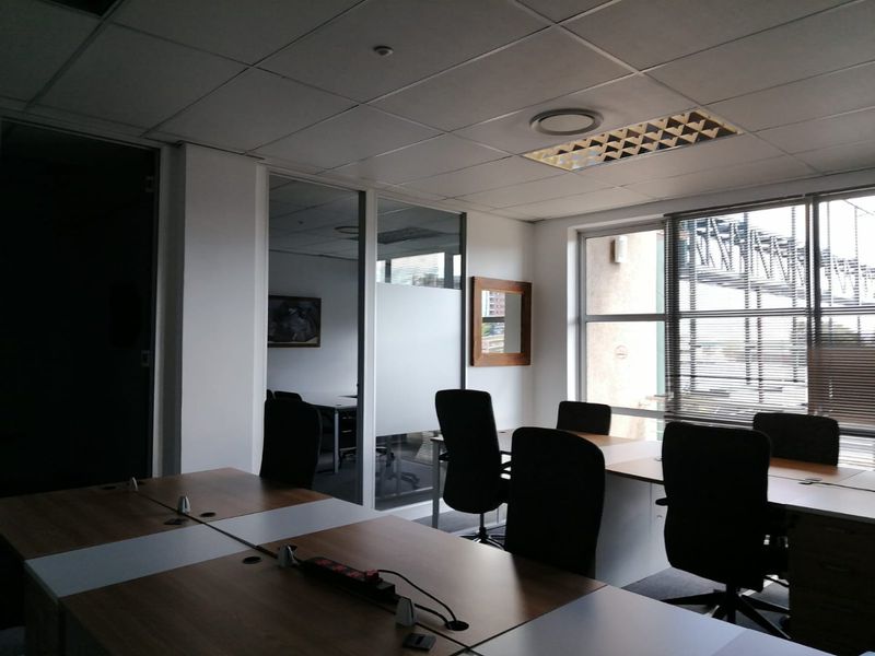 A professional commercial office space featuring a suspended ceiling, glass partitioning for privacy, and large windows that provide ample natural light.