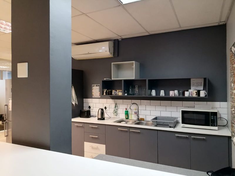 A functional office kitchenette featuring modern grey cabinetry, subway tile backsplash, stainless steel sink, and a wall-mounted air conditioning unit.