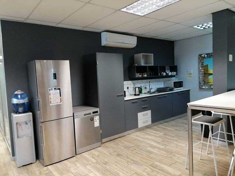 Modern commercial kitchenette featuring dark grey cabinetry, tiled backsplash, stainless steel sink, and integrated air conditioning unit in a professional office environment.