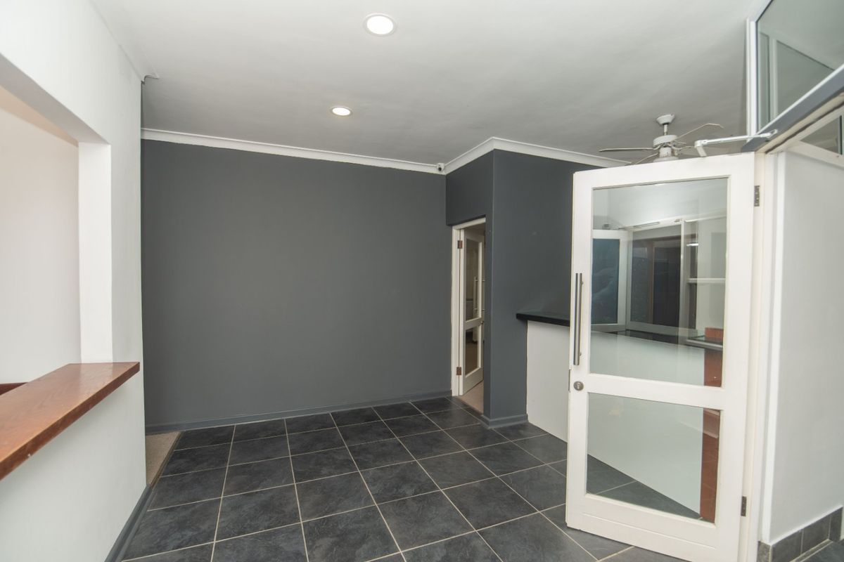 An empty, well-lit commercial space featuring dark tiled flooring, recessed downlights, a ceiling fan, and a glass-paneled door with a serving counter.