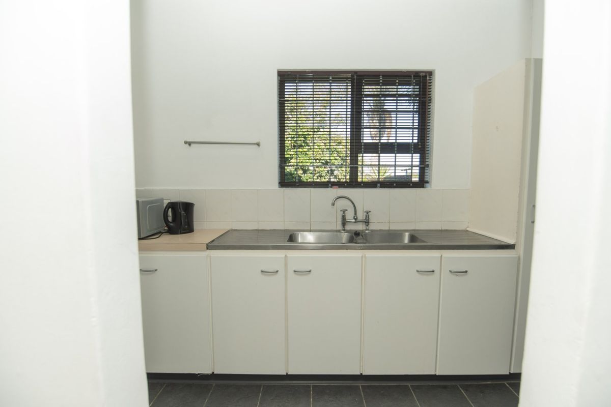 A functional kitchen area featuring a stainless steel double sink, built-in base cabinetry, tiled splashback, and a window with venetian blinds.