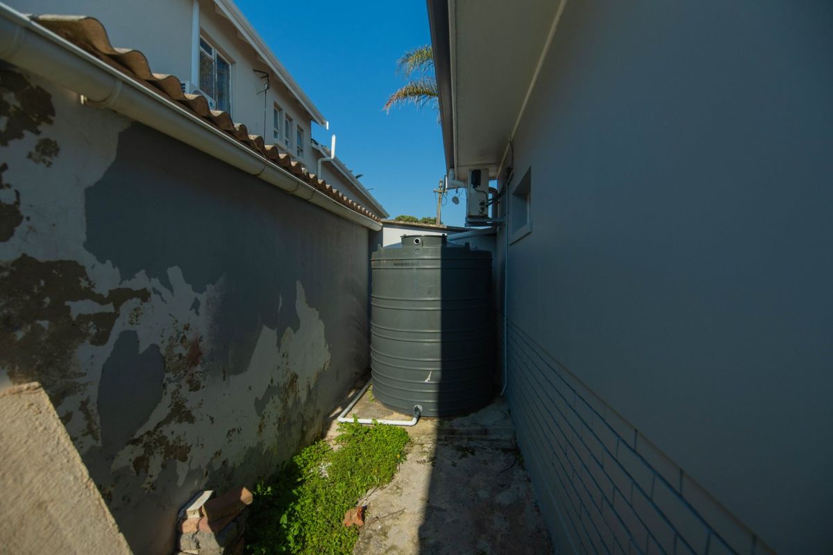 Side alleyway featuring a water storage tank, air conditioning unit, and visible wear to the exterior wall finish.