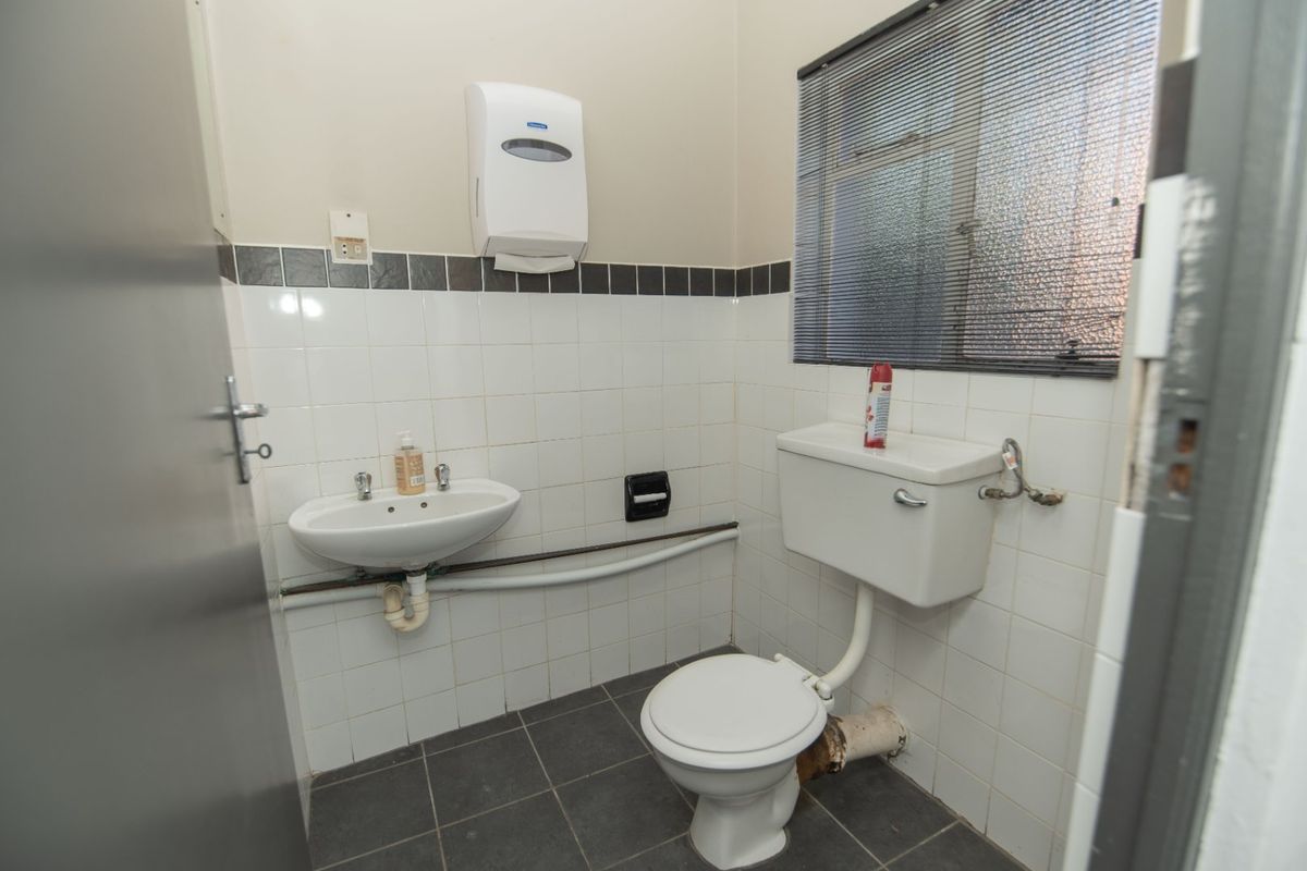 A functional commercial restroom featuring a wall-mounted basin, standard toilet, and tiled splashback, requiring minor maintenance and cosmetic updates.