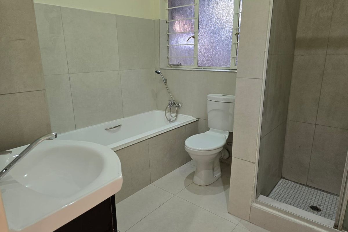 A functional bathroom featuring a bathtub, separate shower enclosure, toilet, and vanity basin with neutral wall and floor tiling.